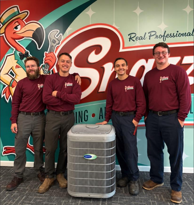 Four Snazzy technicians beside a Carrier air conditioner in front of the Snazzy mural