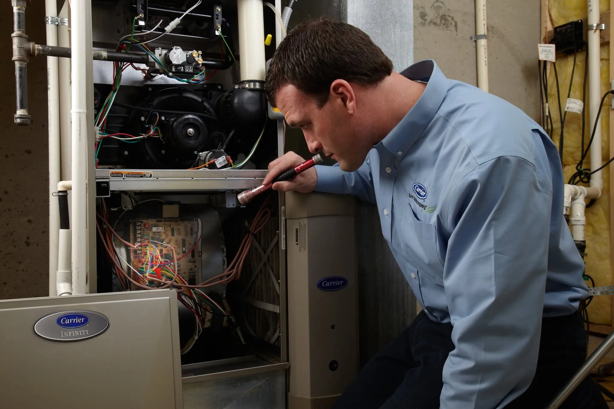 A Snazzy technician inspecting the inside of a furnace with a flashlight